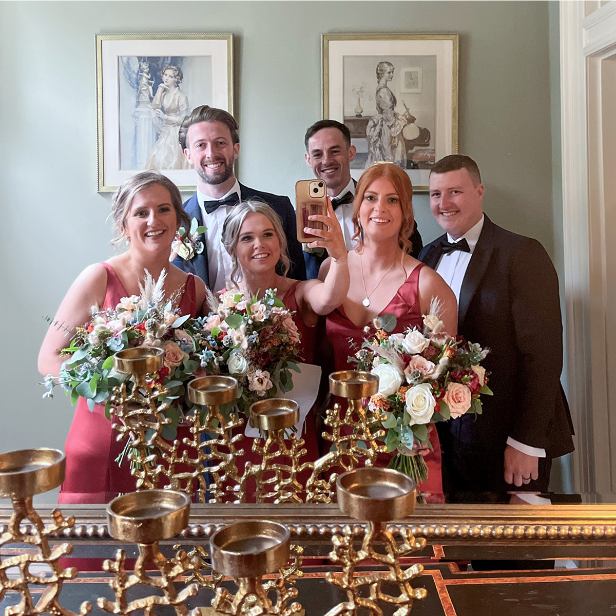 bridal party taking a group selfie using a mirror at a wedding venue